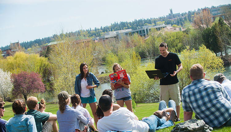 People gather informally by a pond to listen to poetry