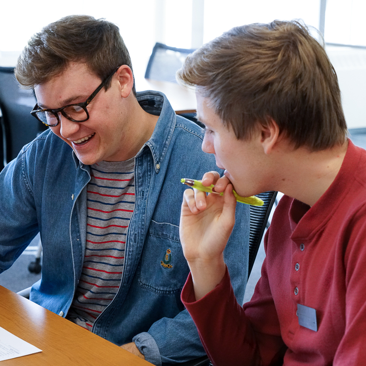 Two students review a document on the table in front of them. One student smiles as the other looks on in friendly contemplation.