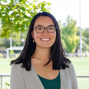 Sarah is wearing a pink Gonzaga standing shirt in front of green bushes