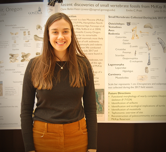 Female student stands proudly in front of her research project board.