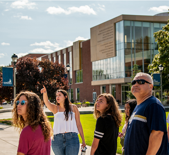 A student tour guide points to something in front of a group of visitors.