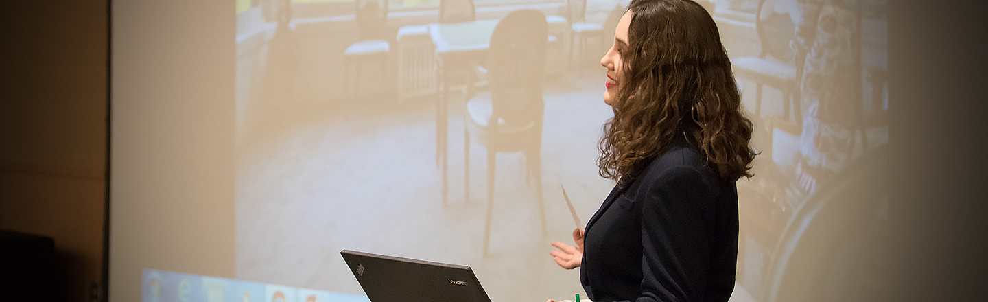 Female lecturer stands in front of large screen projecting image on the topic of digital humanities.