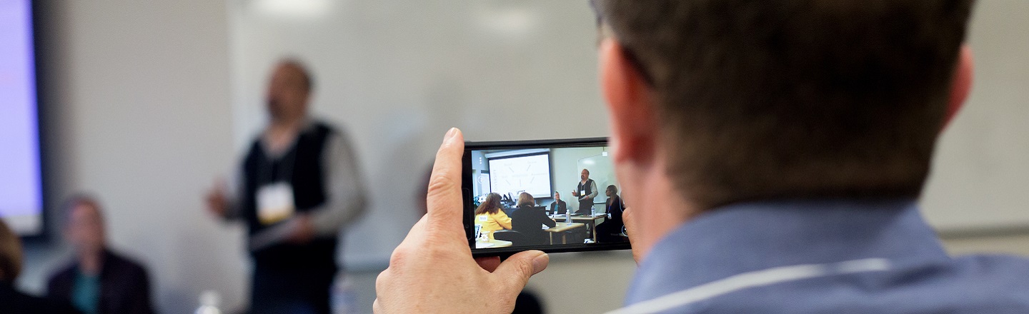 An audience member takes a photo with a smartphone during a presentation. 