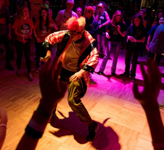 A student dressed as a clown dances in the middle of a circle of people at the Dance Marathon event. 