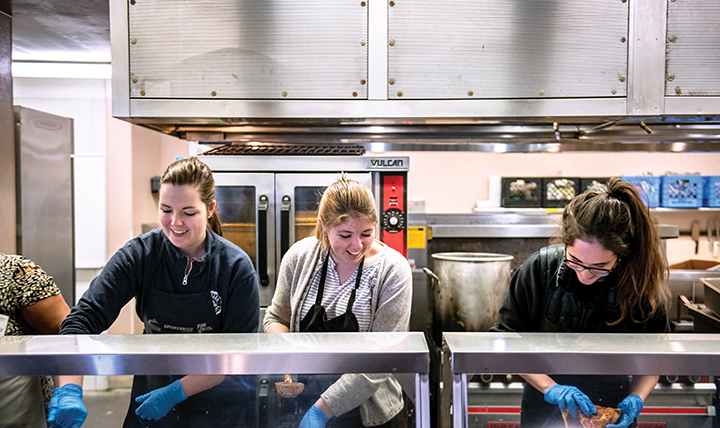 Students work in a food service line at House of Charity. 