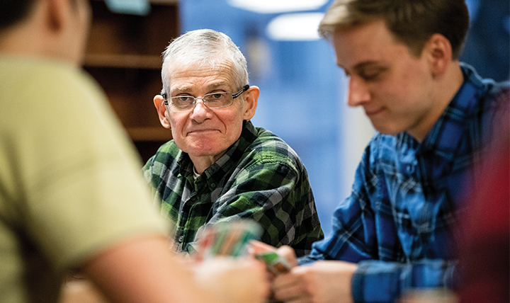 An elderly man plays a game of Uno with two students.