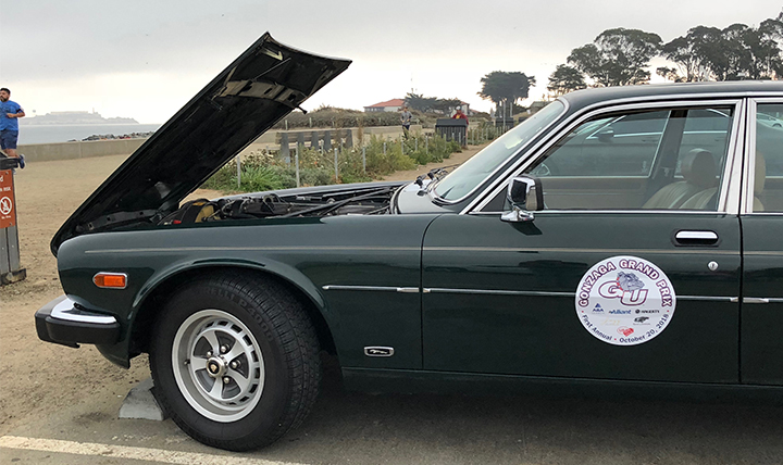 A vintage car with a Gonzaga Bay Area alumni decal with the hood open on the beach.