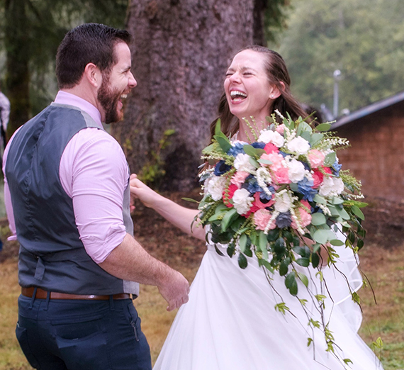 Man and women look at each other in a forest in wedding outfits.