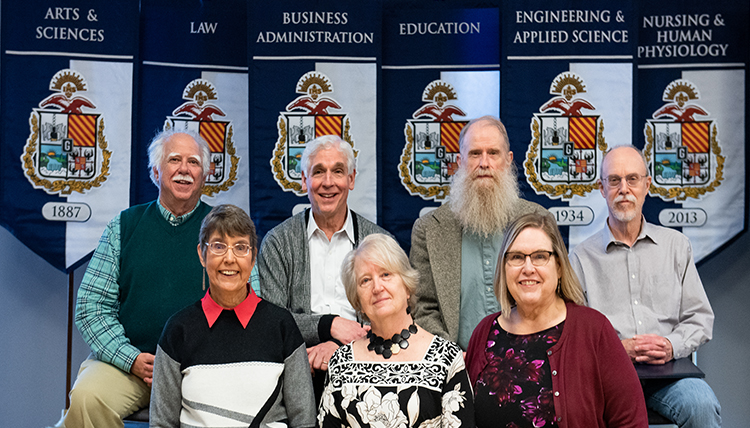 four men stand behind three women, all faculty