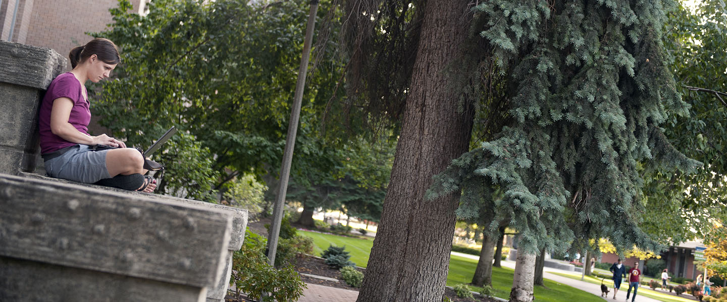 student reads in front of college hall 